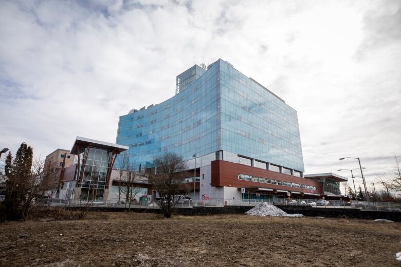 A glass, cube-shaped building is pictured against a cloudy sky.