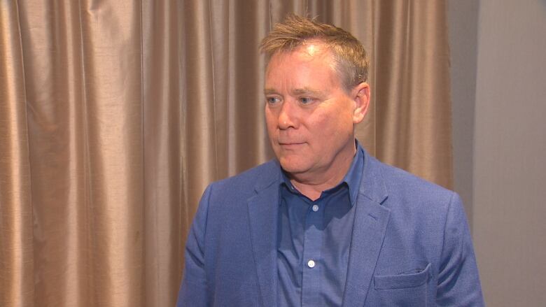 A man with spikey hair in a blue shirt and blazer looks off-camera.