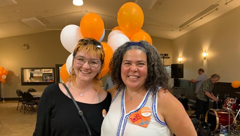 Sarah Elmiligi, wearing a white dress and a blue trim, smiles next to a supporter at her campaign headquarters, filled with white and orange balloons. 