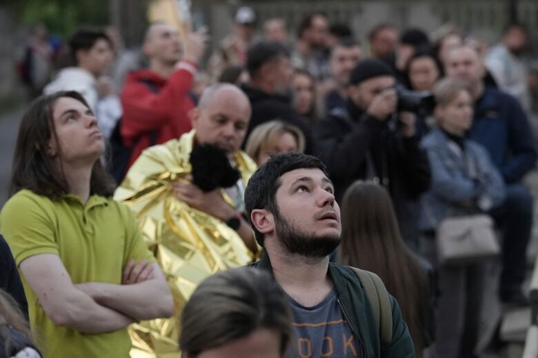 Several people are shown standing outside, with some looking upward.