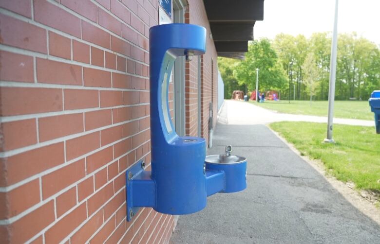 A blue wall mounted water fountain juts out of a the side of a building in a Toronto park. 