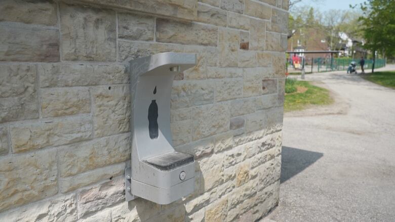 An outdoor water bottle filling station is mounted against a stone wall at a Toronto park. 