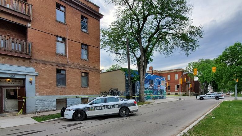 A street scene shows two police cars and yellow police tape across two buildings.