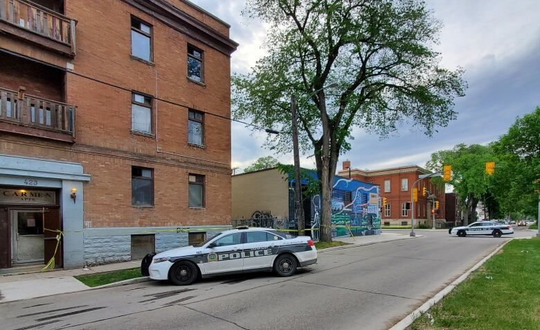 A street scene shows two police cars and yellow police tape across two buildings.