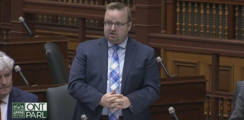 A man stands in front of a microphone wearing a suit. 