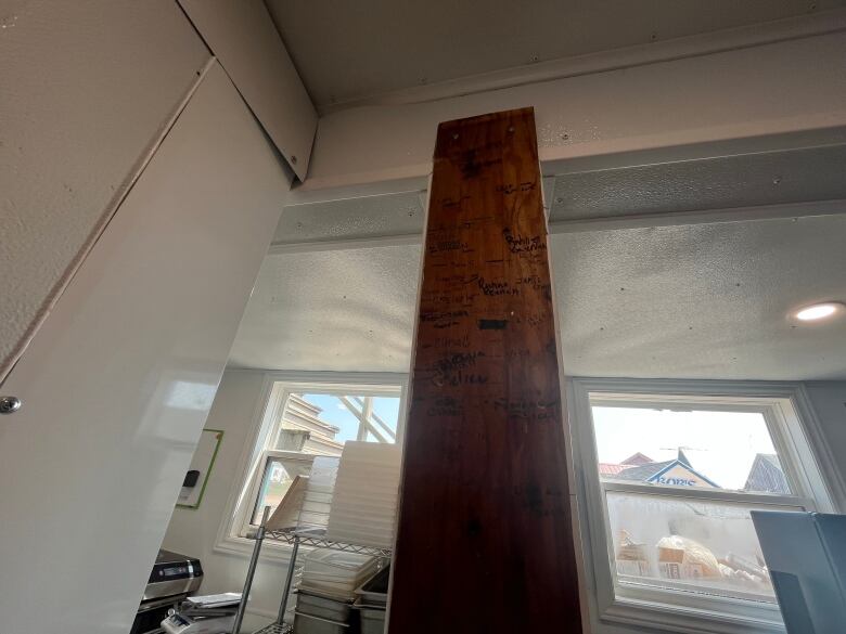 A plant of wood runs vertically up a plastic beam. It is stained wood and stands out against the rest of the white, plastic kitchen.