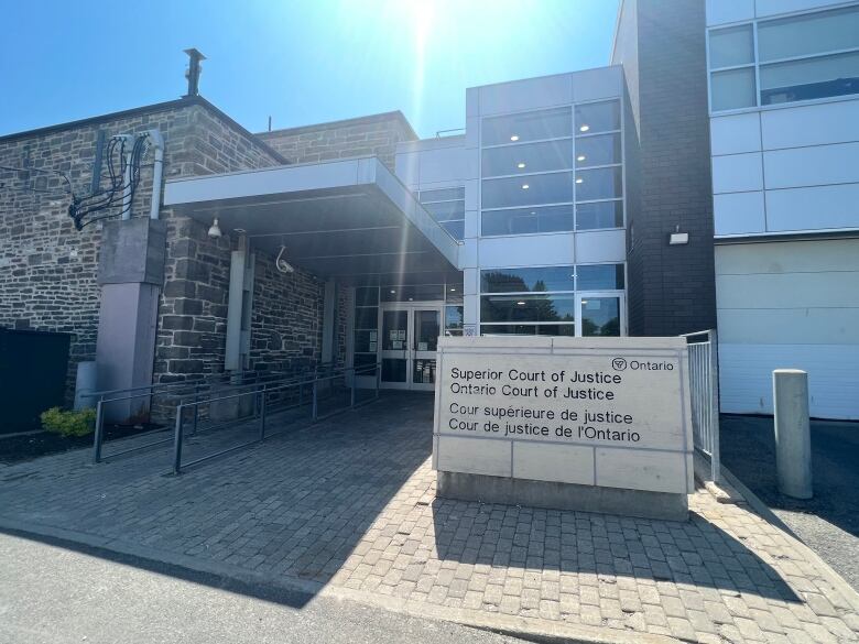 A glass and brick building with a sign out front identifying it as a courthouse is shown on a bright, sunny day.