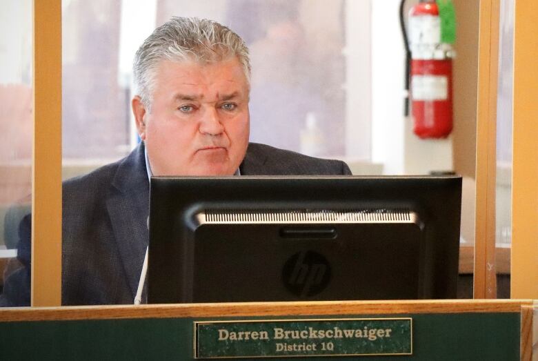 A man with grey hair sits in a cubicle and stares out.