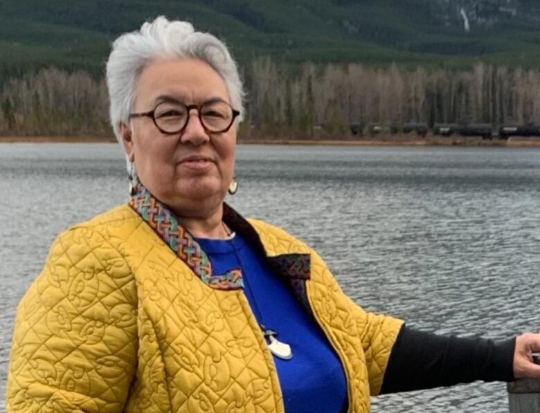 A woman stands by a lake.