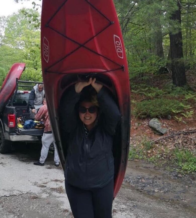 A woman carries a kayak over her head.