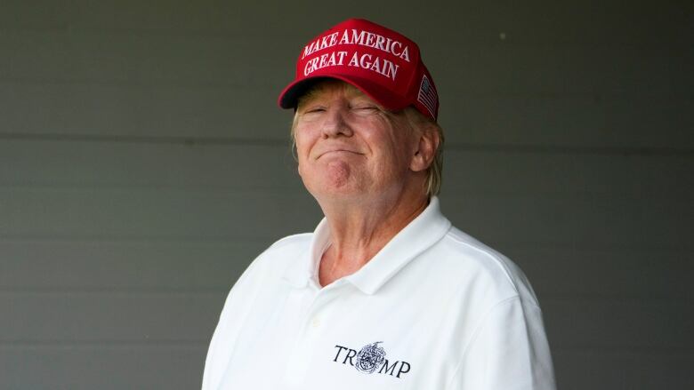 A man in a baseball cap and golf shirt is shown grimacing.