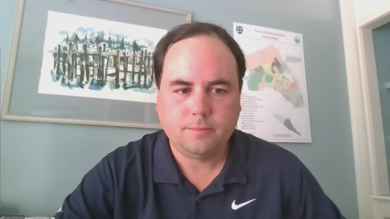 A man wearing a dark blue Nike shirt with a piece of artwork behind him on the left and a map hung up next to it on the right