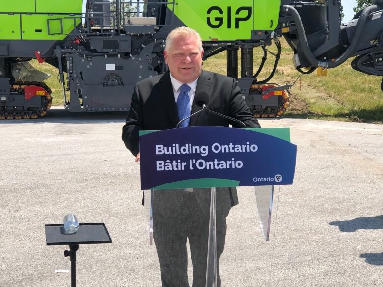 Doug Ford stands at a podium in front of road equipment. 