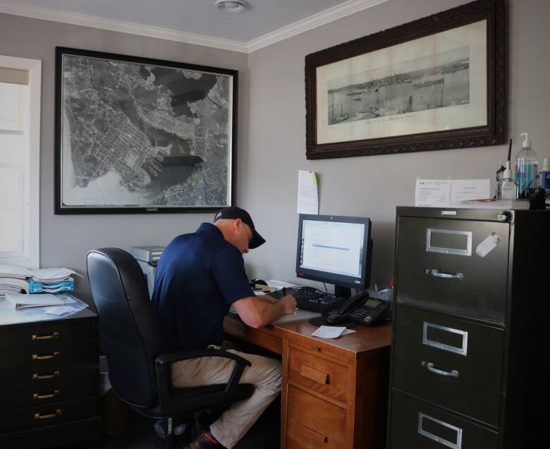 A man in a baseball hat sits in an office filling out paperwork.