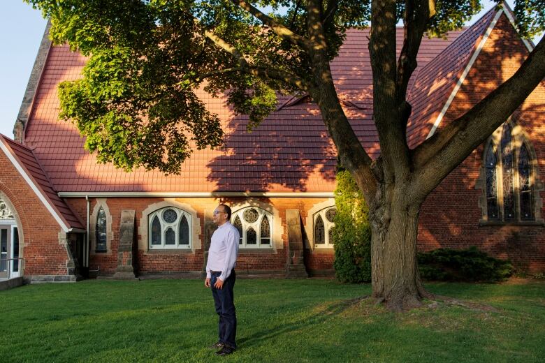 A priest stands outside of a church looking to the side.