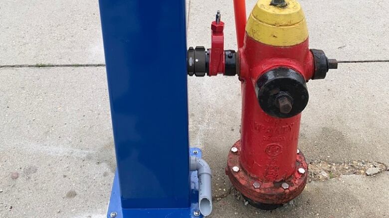 A red fire hydrant with a yellow top is connected to a blue water stand.