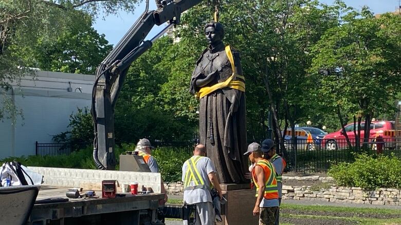 A group of men work to put a statue of a woman back up.