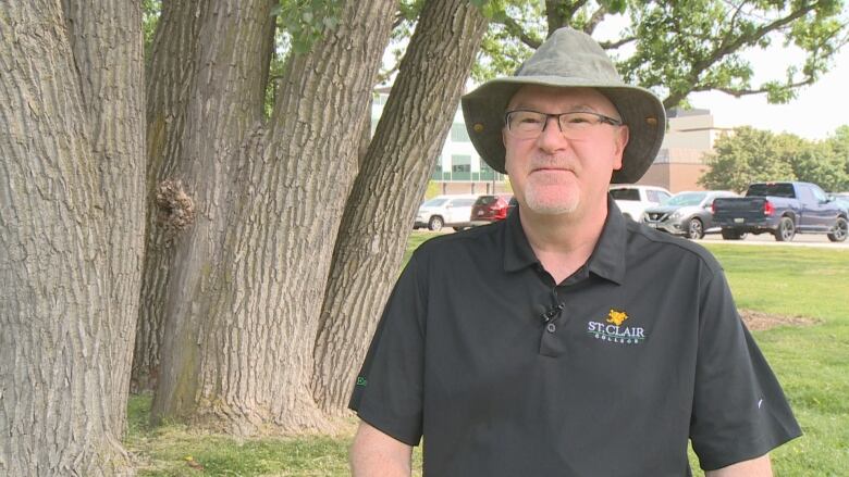 A man in a black shirt stands near a tree. 