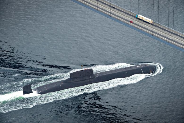 A nuclear submarine travels under a bridge.