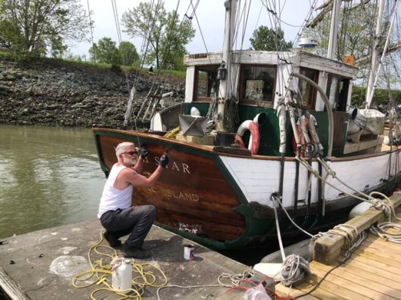 A man applies varnish to the stern of a sailing ship.