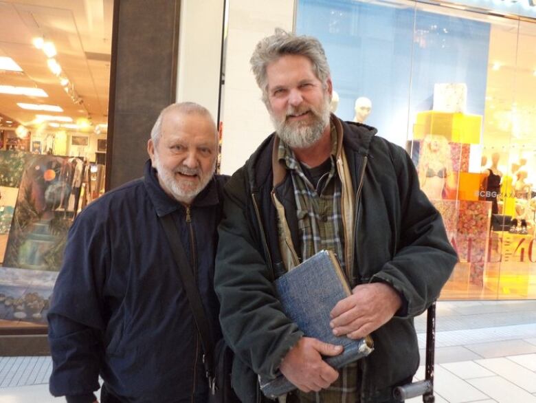 Two smiling men stand in front of a store window.