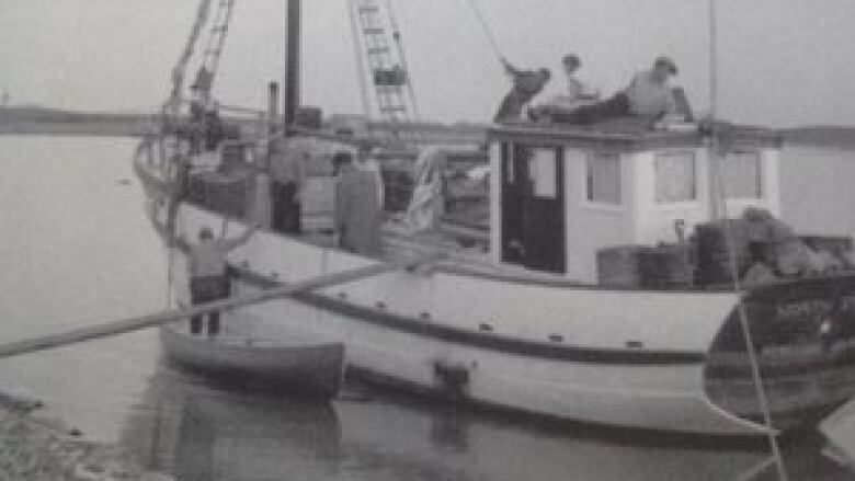 A black and white photo of a sailing ship being loaded up.