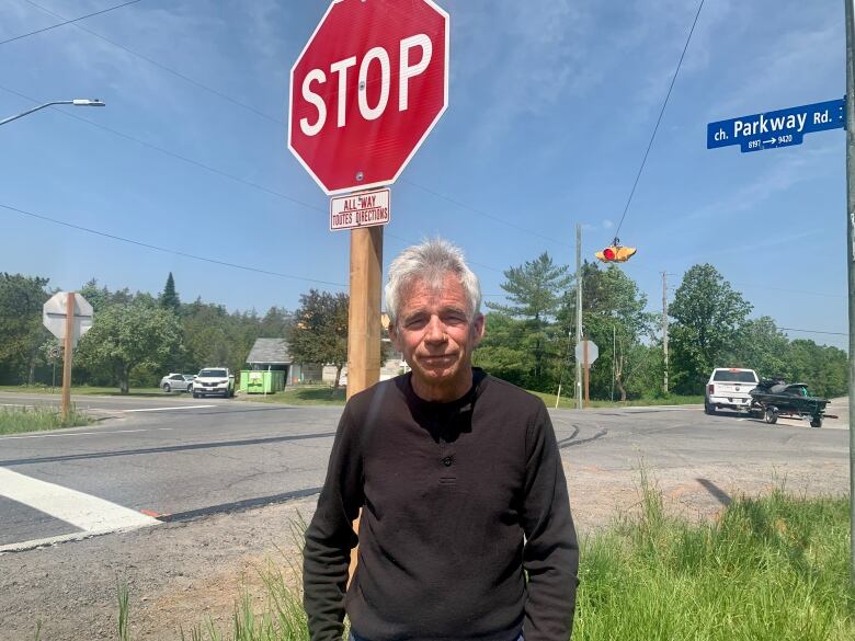 A man stand under a stop sign on a rural road.