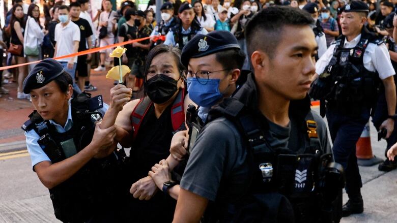 A person holding up a paper flower is detained and led away by police.