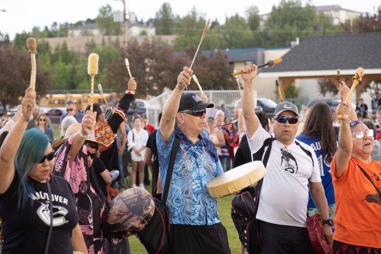 People hold up their traditional drumsticks at an outdoor vigil.