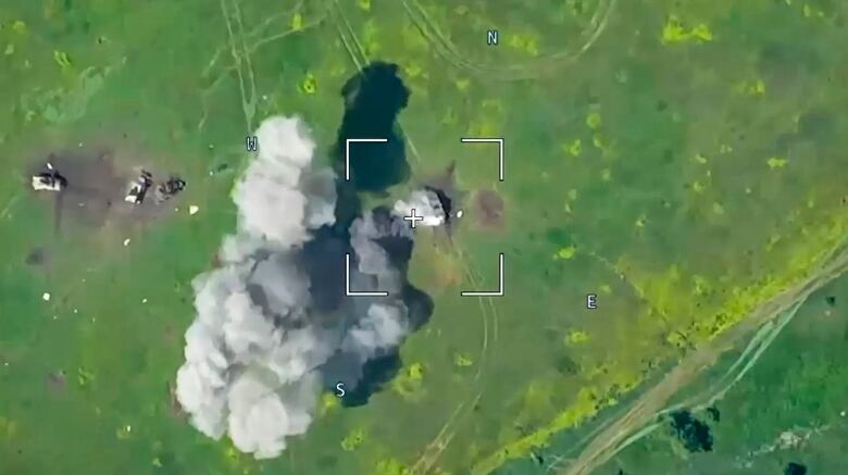 An aerial view from a video shows large clouds of smoke rising from an unspecified object located in a grassy area.