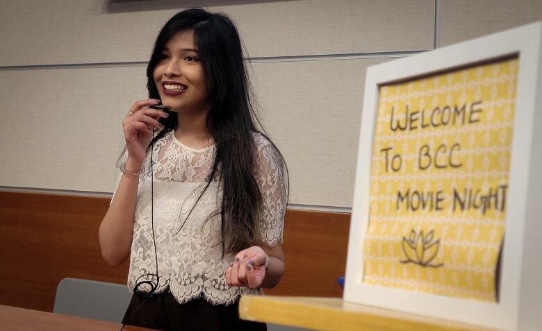 A woman speaks into a lapel microphone, standing beside a sign that reads Welcome to BCC Movie Night.