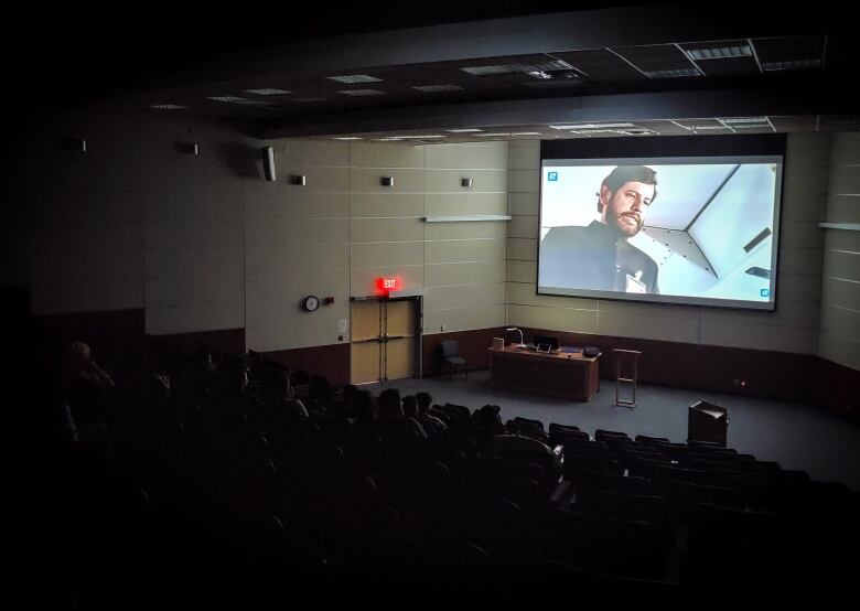 A movie plays on a big screen in a darkened theatre.