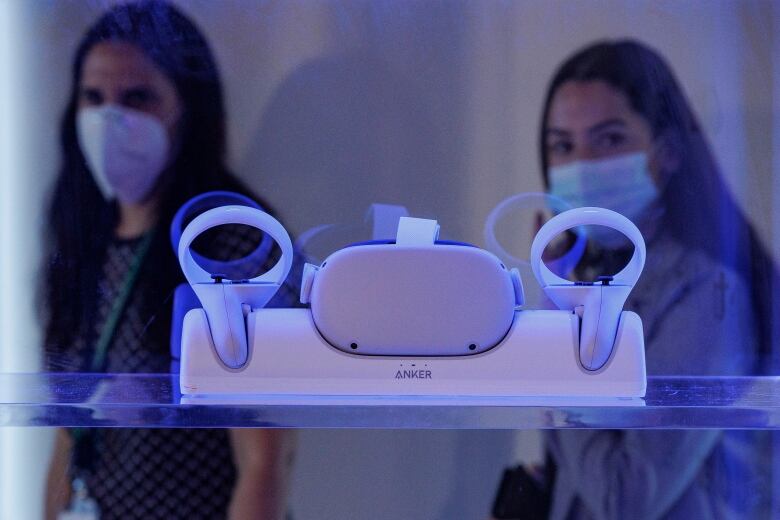 Two women look at a virtual reality headset through a window.