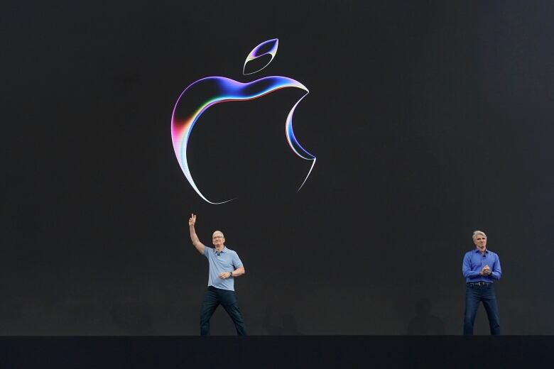 Two men stand in front of the Apple logo.