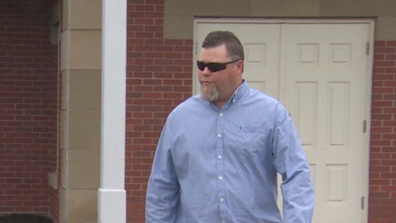 A man wearing a blue dress shirt walks away from a building.