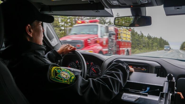 A conservation officer is behind the wheel of a car passing a fire truck on a roadway.