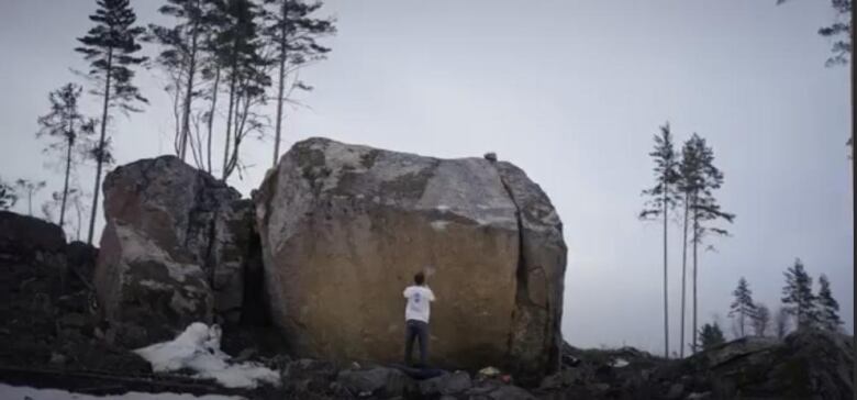 A man stands facing a bounder that's a little more than twice his height.