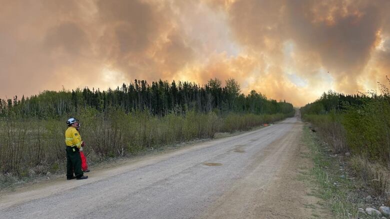 A fireman can be seen standing on a road and looking at the wildfire smoke in the distance. 