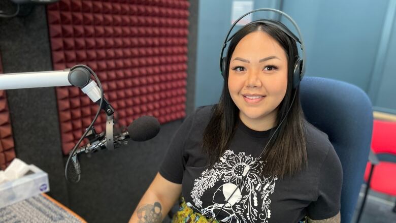 A woman in a bright yellow skirt is pictured sitting in a radio show room with headphones on. 