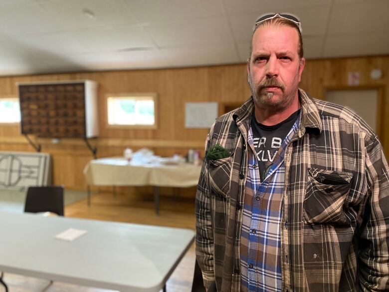 A man stands looking into the camera inside a community hall. 