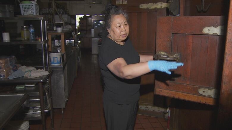 Grace Chen is standing in a dark kitchen in front of an open wooden food storage cabinet. 