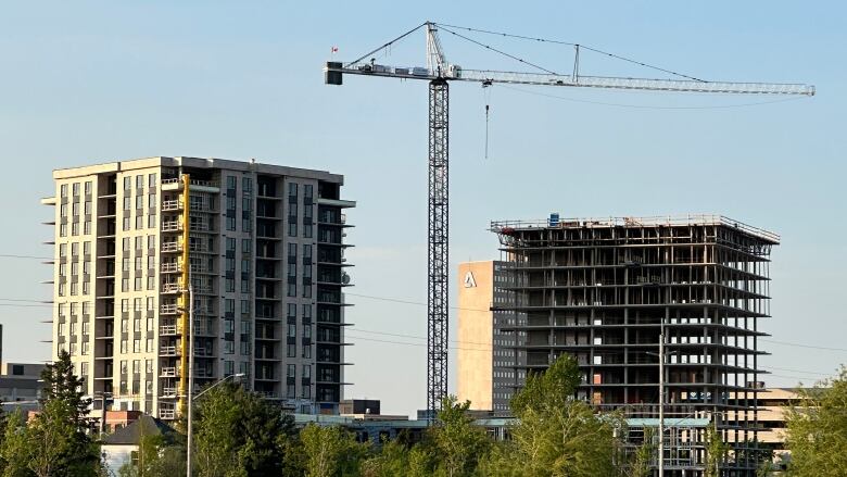 A crane looms over two partially constructed buildings with trees in the foreground.