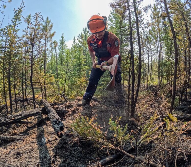 A firefighter uses an axe-like tool to hack at the soil.