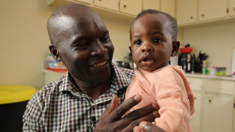 A man smiles at his infant daughter as he holds her in his arms.