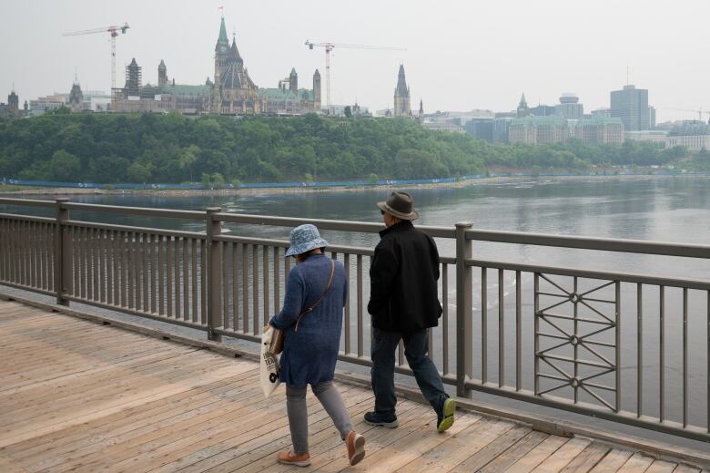 Two people walk a bridge between cities on a smoky day.