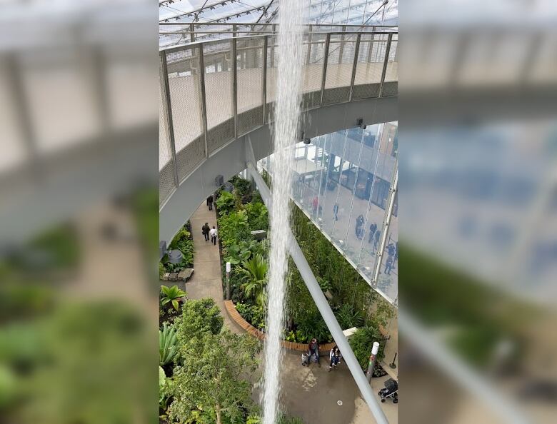 An indoor waterfall falls from a tower and people walk in the distance.