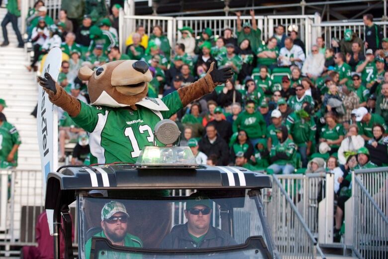 A gopher mascot hanging out of the top of a golf cart raises his arms to hype up a crowd.