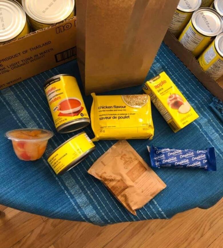 A can of soup, a fruit cup, a granola bar, a can of tuna and a package of oatmeal are displayed below a brown paper bag.