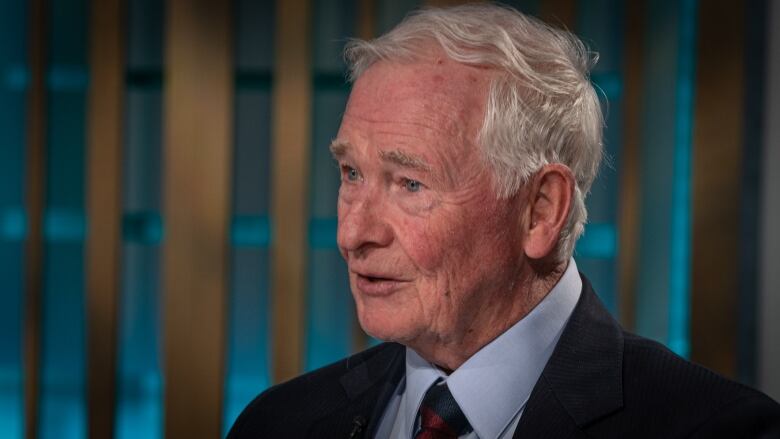 A man in a dark suit answers questions in a television studio.