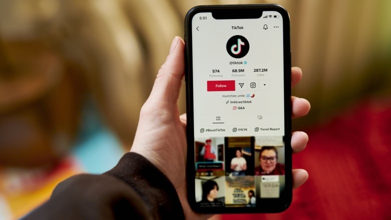 A hand holds up a smartphone with the TikTok app open